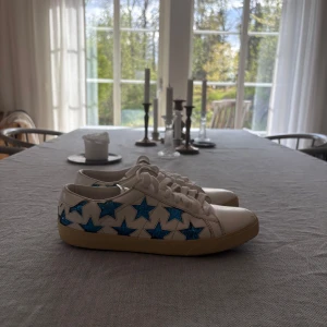 Saint Laurent skor - Säljer ett par ikoniska sneakers från Saint Laurent Paris i storlek 37.5 men sitter som 39. Vita lädersneakers dekorerade med blå glitterstjärnor, en unik och snygg modell som inte säljs överallt. 	•	Äkta skinn 	•	Bekväm passform 	•	Använda men i mycket fint skick, se bilder för detaljer 	•	Sula med viss slitage, ovandel i mycket bra skick 	•	Obs! Originalförpackning eller kvitto medföljer ej  Nypris ca 5 000 kr. Mitt pris: 1 299 kr  Skicka gärna meddelande vid frågor😊