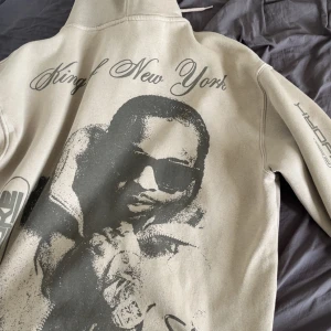 Beige hoodie Pop Smoke King of New York - Säljer en beige hoodie från Pull&Bear med stort Pop Smoke-tryck och texten 'King of New York' på ryggen och ärmen. Hoodien har huva och tryck även framtill. Perfekt för dig som gillar streetwear och unika prints.