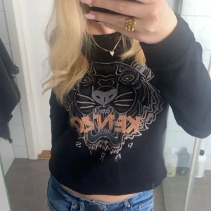 Svart sweatshirt från Kenzo med tigertryck - Svart sweatshirt från Kenzo med stort tigertryck och logga framtill. Tröjan har rund halsringning och långa ärmar. Perfekt statement-plagg för dig som gillar streetstyle.