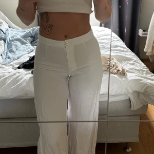 Vita linnebyxor från H&M - Säljer ett par vita linnebyxor från H&M med normal passform och raka ben. Byxorna har hög midja och stängs med knapp och dragkedja framtill. Perfekta för varmare dagar och enkla att matcha med olika toppar.