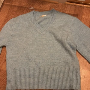 Ljusblå stickad tröja med v-ringning - Mysig ljusblå stickad tröja med v-ringad hals och bred ribbad kant nedtill. Perfekt för kyliga dagar och enkel att matcha med jeans eller kjol.