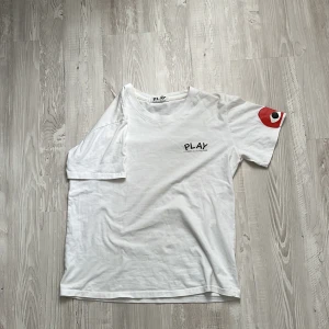 Cdg t shirt - Vit t-shirt från Comme des Garçons Play med svart logga på bröstet och det klassiska röda hjärtmotivet med ögon på ärmen. Rund halsringning och normal passform. Perfekt för en stilren och trendig look. Säljs för 300kr efterslm den här en liten defekt vid armen men kan tänka mig gå ner i pris 