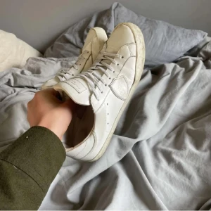 Phillipe Model vita - Säljer ett par klassiska vita sneakers med snörning och rund tå. Skorna har en platt sula och är tillverkade i syntetmaterial. Perfekta för en clean och stilren look.