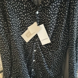 Svart skjorta med vita prickar från Lindbergh - Säljer en svart skjorta från Lindbergh med vita prickar och slim fit-passform. Skjortan har långa ärmar och knäppning framtill. Perfekt för dig som vill sticka ut lite extra med ett snyggt mönster.