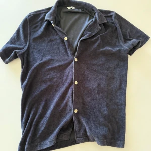 Mörkgrå frottéskjorta från East West - Säljer en mörkblå frotté ifrån brothers med klassisk krage och vita knappar framtill. Perfekt för en avslappnad och trendig look. Väldigt bra skick och säljer då den inte kommer till användning. Pris kan diskuteras vid snabb affär!