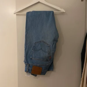 Levis 501 ljusblå jeans W31 L32 - Klassiska Levis 501 jeans i ljusblå denim med raka ben och normal passform. Byxorna har fem fickor, knappgylf och en liten lagning på ena benet. Perfekta för dig som gillar tidlös stil och vintagekänsla.