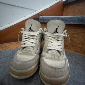 Nike Air Jordans Off-White i beige - Säljer ett par Nike Air Jordans Off-White i beige med vita detaljer och svart logga. Skorna har snörning, meshpaneler på sidorna och texten 'AIR' vid sulan. Klassisk siluett med platt sula och rund tå. Perfekta för dig som gillar streetwear.