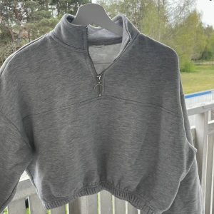Grå croppad sweatshirt med dragkedja från Even&Odd - Grå croppad sweatshirt från Even&Odd med halv dragkedja och hög krage. Tröjan har långa ärmar med resår vid ärmslut och nederkant för en avslappnad passform.