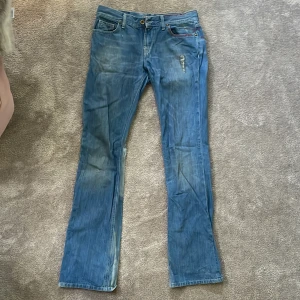 Blå jeansbyxor från Fornarina med röda detaljer - Säljer ett par skitsnygga jeans från Fornarina med röda sömdetaljer och slitningar framtill. Unika jeans som är bootcut men drar lite åt det bredare hållet.