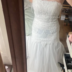 Vit bröllopsklänning från Lilly i st 36 - Säljer en vit långklänning från Lilly med vacker spets och broderade detaljer. Klänningen är axelbandslös med snörning i ryggen och har en romantisk, figurnära passform. Perfekt för speciella tillfällen. Klänningen är testat ett par gånger hemma men aldrig använd på något speciellt tillfälle! Den har inga defekter och är inprincip ny förutom att den legat i garderoben i över 1 år🥰🥰Säljer den för 4999kr + frakt då den inte är använd samt slutsåld i just denna modellen! Nypris är 5599