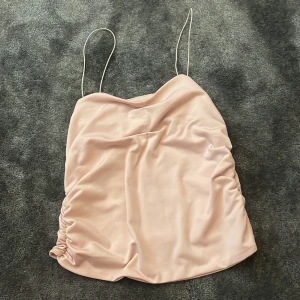 Ljusrosa satinlinne med tunna axelband - Säljer ett ljusrosa linne i satin med tunna axelband och rynkade sidor.