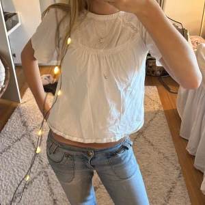 Vit blus med broderad detalj - Säljer en söt vit blus med korta ärmar och rund halsringning. 