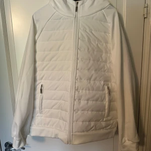 Cardigan  - Säljer en vit hoodiejacka med quiltade partier och dragkedja framtill. Jackan har två fickor med dragkedja och en mysig huva. Perfekt för dig som gillar en stilren och sportig look. Oanvänd och Cond är 10/10 den är princip ny. Vid fler frågor eller funderingar är det bara att höra av dig!