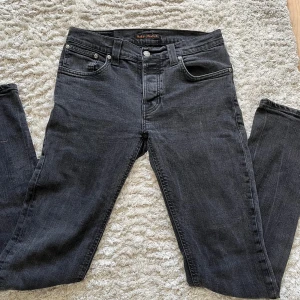 Nudie jeans Grim Tim - Säljer ett par svarta jeans från Nudie Jeans i modellen Grim Tim med klassisk femficksdesign och raka ben. Jeansen har slim fit passform och är tillverkade i denim. Perfekta för dig som gillar stilrena och tidlösa byxor. Jeansen är i storlek W29/L32 men storlekslappen har tyvärr försvunnit.