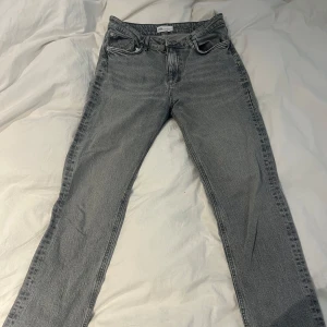 Grå jeansbyxor från Zara - Säljer ett par klassiska grå jeans från Zara med fem fickor och raka ben. Jeansen har normal passform och stängs med dragkedja och knapp. Perfekta till vardags för en stilren look.