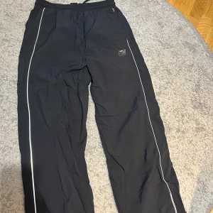  Vintage byxor med reflex  från Frans - Säljer ett par svarta träningsbyxor från Frans med vita ränder längs benen. Byxorna har resår i midjan och vid bensluten, samt en sportig look som passar perfekt till gymmet eller löprundan.