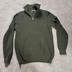 Olivgrön stickad tröja med dragkedja från Zara - Storlek M. Säljer en olivgrön stickad tröja från Zara med halv dragkedja och hög krage. Tröjan har lång ärm och ribbade muddar vid ärmslut och nederkant. Perfekt för lager-på-lager och snygg till jeans eller chinos.