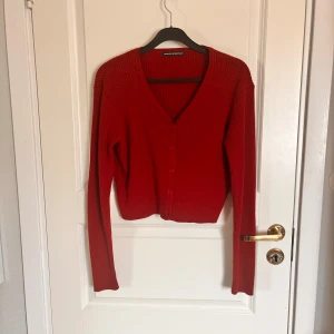 Röd ribbad kofta från Brandy Melville - Säljer en röd croppad kofta från Brandy Melville. Tröjan är ribbad, har v-ringning och knappar framtill. Långärmad och perfekt att styla till olika outfits. Superenkel att matcha och riktigt snygg färg!