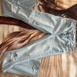 Ljusblå ripped jeans från Gina tricot - Säljer ett par ljusblå jeans från Gina tricot med snygga slitningar på benen. Jeansen har klassisk femficksdesign, dragkedja och knapp framtill. Perfekta för en avslappnad och trendig look.