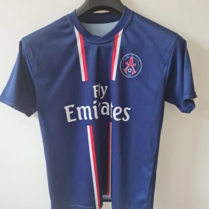 PSG fotbollströja Ibrahimović 18 (barn) - Paris Saint-Germain fotbollströja med röda och vita detaljer, Fly Emirates-tryck på framsidan och Ibrahimović 18 på ryggen. Perfekt för fans av PSG och Zlatan. Bröstmått 92cm. Kan hämtas i Vallentuna.