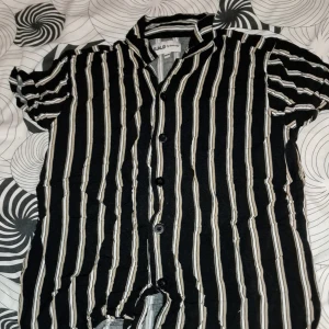 Svart och vit randig skjorta från D.M.D - Kortärmad skjorta med svarta och vita vertikala ränder från D.M.D by denim day. Skjortan har knappar framtill och klassisk krage. Perfekt för en avslappnad och trendig look.