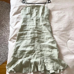 Ljusgrön klänning med volang från Gina Tricot - Säljer en ljusgrön (är något ljusare än vad som framgår i bilden) klänning från Gina Tricot med smala axelband och volangkant nertill. Klänningen har en figurnära passform upptill och är tillverkad i ett linne material. Den går strax ovanför knäna och är i en ljusgrön färg💕