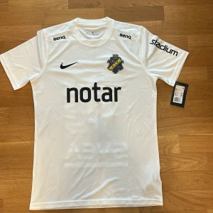 Vit AIK fotbollströja från Nike - Säljer en vit AIK fotbollströja från Nike med svart tryck, klubbmärke på bröstet och sponsorer. Nummer 10 på ryggen och SVEA-tryck. Kortärmad modell i Dri-Fit material, perfekt för match eller träning.