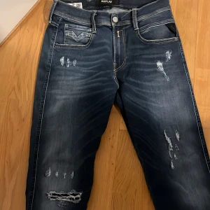 Replay Anbass jeans med slitningar - Säljer ett par mörkblå Replay Anbass hyperflex jeans med snygga slitningar och detaljer på benen. Klassisk femficksmodell med gul kontrastsöm och Replay-logga vid fickan. Slim passform och bekvämt jeansmaterial. Perfekta för dig som gillar en modern look. Hör av dig vid frågor eller funderingar.