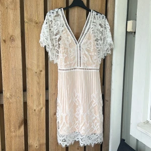 Vit spetsklänning med v-ringning - Superfin vit kortklänning med v-ringad hals och detaljerad spets över hela klänningen. Klänningen har korta ärmar i spets och ett romantiskt mönster. Perfekt för sommarens alla tillfällen! Aldrig använd 💞