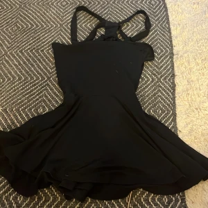 Svart kort klänning med korsade axelband från Chiara Forni - Säljer en svart kort klänning från Chiara Forni i storlek 34. Klänningen har smala korsade axelband och en utställd kjol som ger en snygg siluett. Perfekt för dig som gillar stilrena och enkla plagg med en twist.