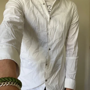 Vit skjorta från Riley Super Slim Fit - Klassisk vit skjorta från Riley i super slim fit-modell. Skjortan har långa ärmar, knappar framtill och en stilren design som passar perfekt till jeans eller kostymbyxor. Tillverkad i ett tunt och lätt material för en fräsch look.