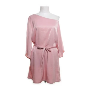 Ljusrosa omlottklänning i satin  - Säljer en ljusrosa kortklänning i satin från NA-KD x Hannelisious Klänningen har en offshoulder-design, trekvartsärm och knytskärp i midjan för en snygg passform. Perfekt för dig som gillar en feminin och stilren look.