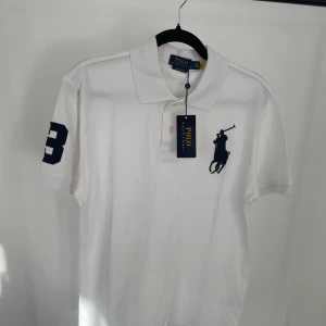 Polo Ralph Lauren pike - Vit pikétröja från Polo Ralph Lauren med klassisk krage och knappar framtill. Stor broderad logga på bröstet och en stor mörkblå siffra 3 på ena ärmen. Slim fit-modell i bomull, perfekt för sommaren