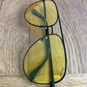 Svarta pilotglasögon med gula glas från Quay - Snygga pilotbågar i svart metall med gula tonade glas från Quay. Perfekta för att sticka ut och ge en cool look. Lätta och bekväma att bära, passar både till vardag och när du vill ha något extra. Lite spricka i glaset finns.