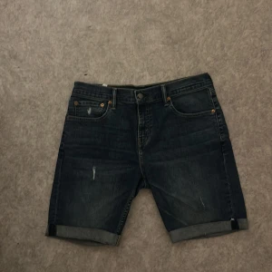 Mörkblå jeansshorts från Levi's - Säljer ett par klassiska mörkblå jeansshorts från Levi's med fem fickor och uppvikta benslut. Shortsen har en normal passform och är tillverkade i slitstarkt denim. Perfekta för sommaren!