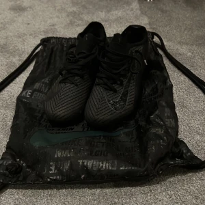 Nike mercurial vapor 16 elite - Säljer ett par svarta Nike fotbollsskor med snyggt mönster och glansig Nike-logga på sidan. Skorna har snörning och låg profil, perfekta för dig som vill ha stilrena och sportiga skor på planen. Levereras med svart Nike-påse. Köptes för 3600 säljs för 600