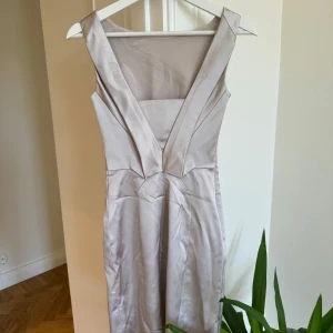 Ljusbeige klänning från Karen Millen - Supersnygg ljusbeige klänning från Karen Millen med omlottdetaljer och markerad midja. Klänningen har breda axelband och en elegant, figurnära passform som framhäver siluetten. Perfekt för speciella tillfällen. Står XS men skulle säga att det passar XXS
