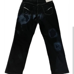 Mörkblå jeansbyxor med stenar från Iber - Unika mörkblå jeansbyxor från Iber med blekta detaljer och dekorativa stenar på bakfickorna. Byxorna har klassisk femficksdesign och raka ben. Tillverkade i viskos och elastomer för extra komfort. Snygg italiensk design.