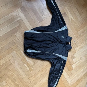 Svart jacka från Erima med vita detaljer - Svart jacka från Erima med vita och grå detaljer längs ärmar och sidor. Väldigt snygg men använder ej. Man kan ändra storlek i modjan! Kan mötas i sthlm, klicka INTE köp nu, skriv privat isf!)