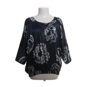 Mörkblå blommig blus från Truly by Part Two - Mörkblå blus i 100% siden från Truly by Part Two. Blusen har ett vitt blommigt mönster, rund halsringning och trekvartsärmar. Resår vid hals, ärmslut och nederkant ger en avslappnad passform.