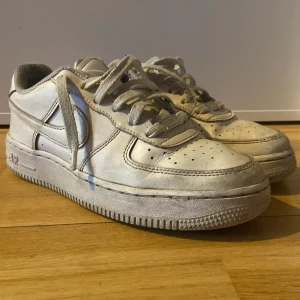 Vita Nike Air Force 1 07 sneakers - Klassiska vita Nike Air Force 1 sneakers med snörning och rund tå. Skorna har en platt sula och är tillverkade i syntetmaterial med detaljer i skinn. Perfekta för en streetwear-look och passar till det mesta.