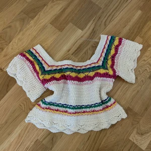 Virkad topp med färgglada ränder - Superfin virkad topp i offwhite med färgglada ränder i rosa, blått, gult och grönt. Toppen har korta ärmar med vågig kant och en bred, rundad halsringning. Perfekt för sommarens alla tillfällen!