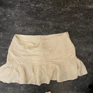 Beige volangkjol från Nelly - Säljer en beige kortkjol från Nelly med volang nertill. Kjolen är tillverkad i ett linneliknande material och har en feminin och luftig känsla. Perfekt för varma dagar och enkel att matcha med olika toppar.