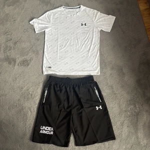  Under Armour set  XL= XS/S - Svarta träningsshorts från Under Armour i storlek  xs/s  Tillverkade i 100% polyester med elastisk midja och snörning. Shortsens design har vita logotyper och dragkedjeförsedda fickor på sidorna, perfekt för gym eller löpning.