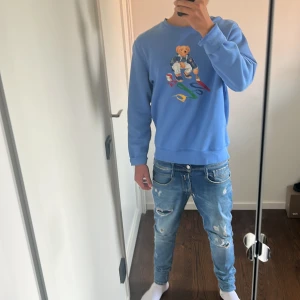 Blå sweatshirt Polo Bear Ralph Lauren - Säljer en blå sweatshirt från Polo Ralph Lauren med ikoniskt Polo Bear-tryck framtill. Tröjan har rund hals, långa ärmar och är gjord i mjuk bomull. Perfekt för dig som gillar streetstyle och vill sticka ut med en färgglad detalj.
