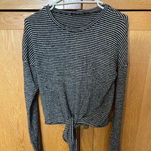 Randig långärmad topp med knyt - Säljer en svartvit randig långärmad topp med rund hals och snygg knytdetalj framtill. 
