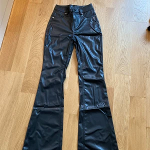 Svarta bootcut byxor i skinbyxor från H&M - Snygga svarta byxor från H&M Divided i skinnimitation. Modellen är bootcut med normal passform och klassiska fickor både fram och bak. 