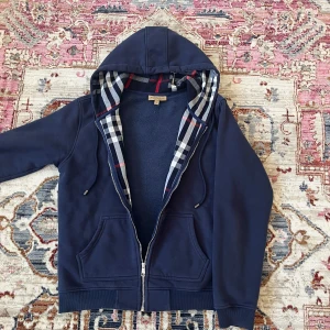 Burberry hoodie - Säljer en marinblå hoodie från Burberry. Säljer den då den inte passar längre. Köptes på plick runt 8 månader sedan. Skriv gärna vid fler frågor. Priset är ej hugget i sten vid snabb affär!!