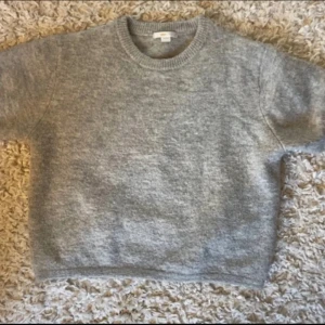 Grå croppad stickad tröja från Gina Young - Mysig grå stickad tröja med croppad passform och kortare ärmar. Perfekt att slänga på sig över ett linne eller t-shirt. Rund halsringning och enkel design som funkar till många olika outfits.