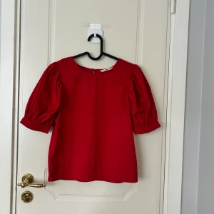 Röd blus med puffärm från Ellos - Snygg röd blus från Ellos med puffiga korta ärmar och rund halsringning. Perfekt för dig som vill ha en färgstark och trendig topp. Tillverkad i mjuk bomull som känns skön mot huden.